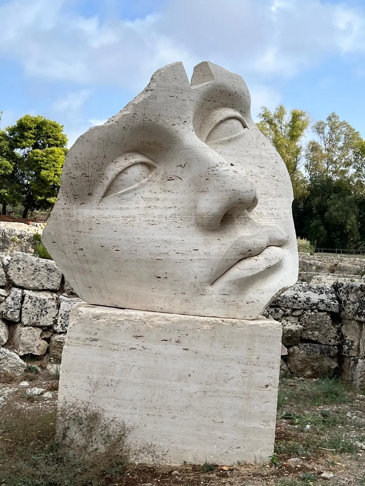 Large stone face sculpture displayed outdoors at an art exhibition in Syracuse